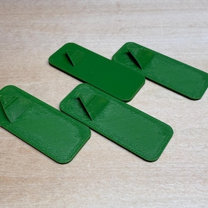 May include: Four green rectangular objects with a textured surface and a triangular raised section on one end. The objects are arranged on a light-colored wooden surface.