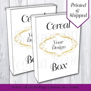 May include: Two white cereal boxes with black text that reads "Cereal Box" and "Your Design" inside a gold ornate frame. The top right corner has a purple banner that says "Printed & Shipped". The website address www.designsbyreginarenee.com is at the bottom.