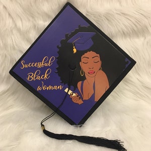 May include: A graduation cap with a black border and a purple background. The cap features an illustration of a Black woman with curly hair and a graduation cap. The words "Successful Black Woman" are written in gold script.
