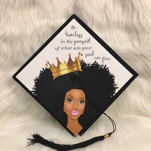 May include: Black graduation cap with a graphic of a woman with a gold crown and the text "Be fearless in the pursuit of what sets your soul on fire." The cap has a black tassel.