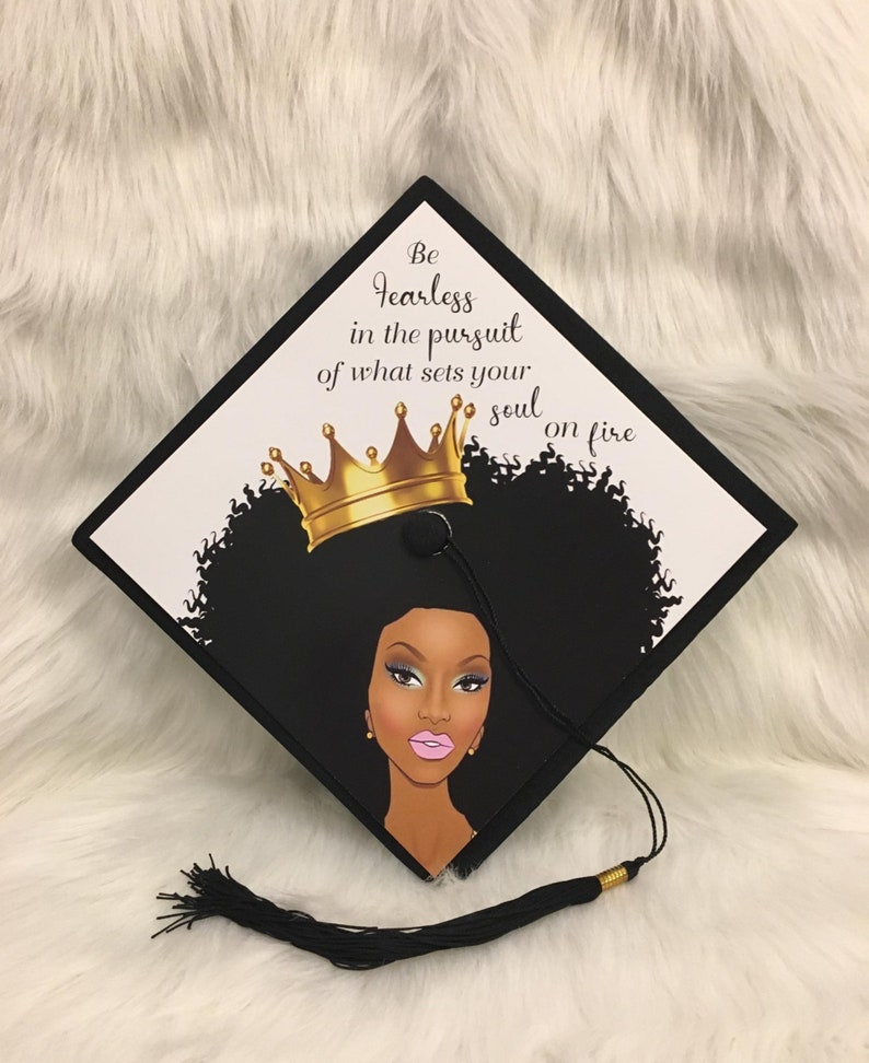 May include: Black graduation cap with a graphic of a woman with a gold crown and the text "Be fearless in the pursuit of what sets your soul on fire." The cap has a black tassel.