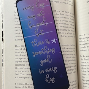 May include: A rectangular bookmark with rounded corners featuring a vertical gradient from purple to dark blue. The text reads: every day may not be good but there is something good in every day, accented with small white stars and horizontal lines.