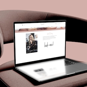 Könnte beinhalten: Ein silberner Laptop zeigt eine Website mit einem Foto einer Person, Text und dem Schriftzug book now! und steht auf einem braunen Polsterstuhl mit geschwungener Rückenlehne und schwarzen Metallbeinen vor einem hellrosa Hintergrund.