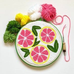 10 inch green plastic embroidery hoop. Pink and yellow lemon slices with green leaves. Mini skeins of yarn in pink, white, yellow and green colors. Punch needle next to it.