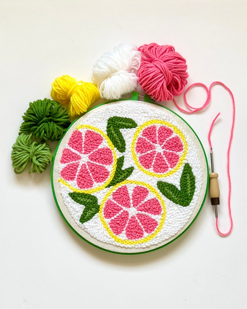 10 inch green plastic embroidery hoop. Pink and yellow lemon slices with green leaves. Mini skeins of yarn in pink, white, yellow and green colors. Punch needle next to it.