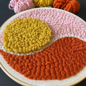 May include: A round embroidery hoop with a pink, orange, and yellow yarn design. The yarn is woven into a geometric pattern.