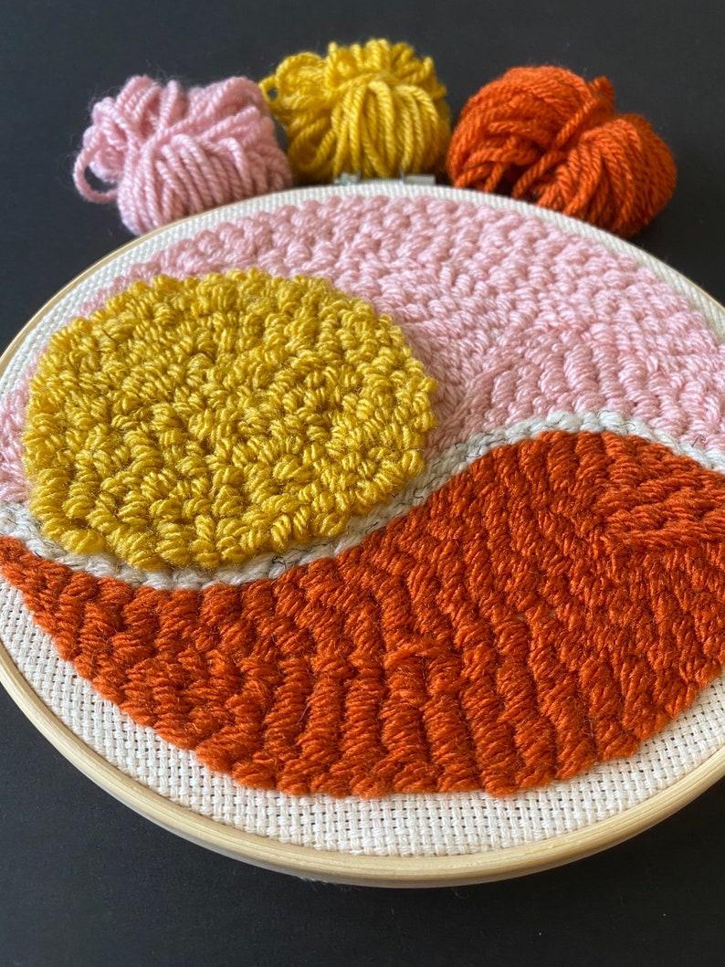 May include: A round embroidery hoop with a pink, orange, and yellow yarn design. The yarn is woven into a geometric pattern.
