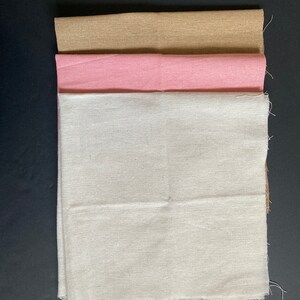 May include: Three fabric squares stacked on top of each other. The top square is a light brown color, the middle square is pink, and the bottom square is white.