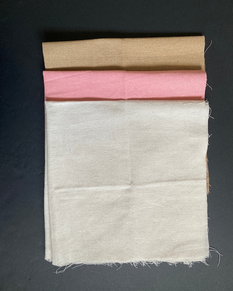 May include: Three fabric squares stacked on top of each other. The top square is a light brown color, the middle square is pink, and the bottom square is white.