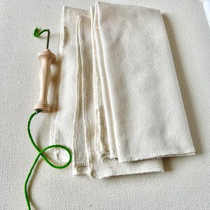 May include: A wooden needle threader with a green thread and a white fabric background.