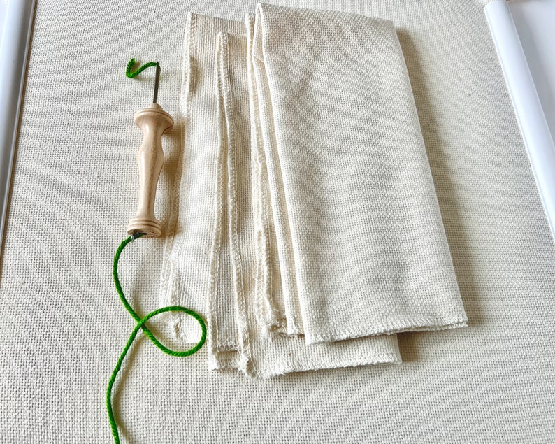 May include: A wooden needle threader with a green thread and a white fabric background.
