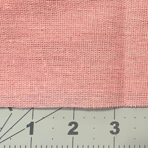 May include: Close-up of a pink fabric with a woven texture. The fabric is measured with a ruler showing 1, 2, and 3 inches.