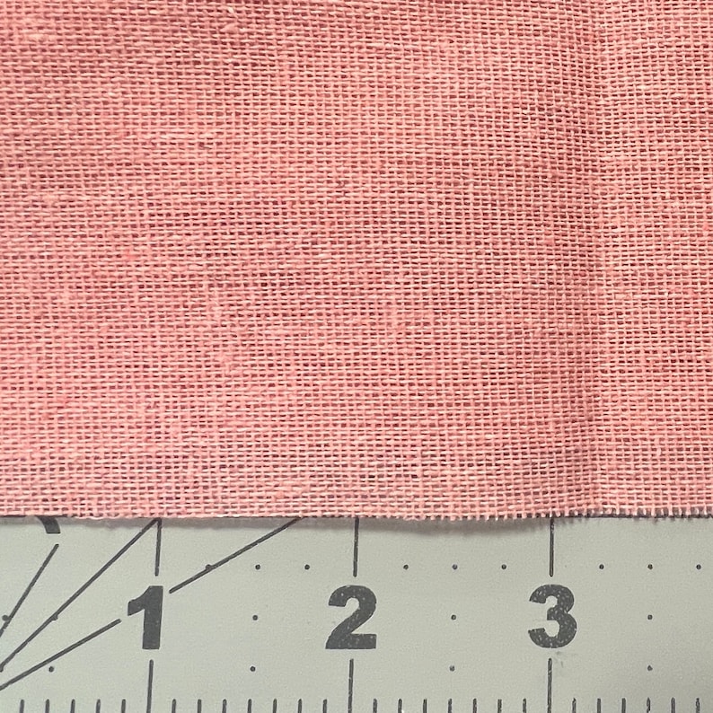 May include: Close-up of a pink fabric with a woven texture. The fabric is measured with a ruler showing 1, 2, and 3 inches.