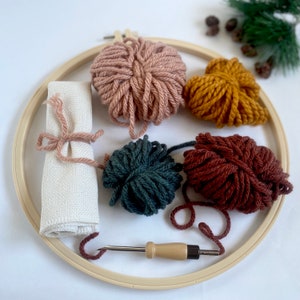 12 inch plastic embroidery hoop, 4 mini skeins of yarn in pink, yellow, brown, green. Rolled monks cloth tied with pink yarn. lavor 5.5mm punch needle