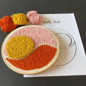 May include: A completed punch needle embroidery hoop with a geometric design in pink, yellow, and orange. The hoop is on a white sheet of paper with the text "Punchy Stuff Studio" printed on it.