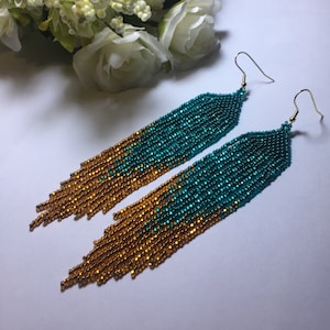 May include: A pair of long, beaded earrings with a gradient of gold and teal colours. The earrings are made with small, round beads and have a tassel-like design.