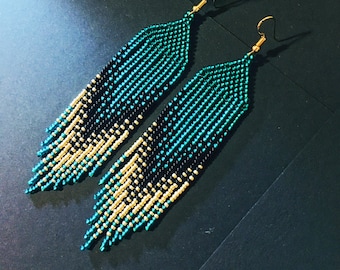 May include: A pair of long, beaded earrings with a gradient of gold, black, and teal beads. The earrings are made with small, round beads and have a tassel-like design.