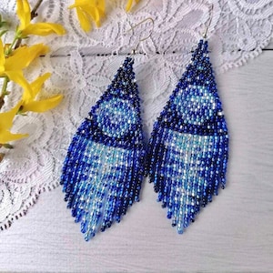 May include: A pair of long, teardrop-shaped earrings made with blue and silver beads. The earrings have a fringe design and are hanging from silver hooks.
