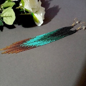 May include: A pair of long, beaded earrings with a gradient of colors, starting with gold, then brown, turquoise, green, and black. The earrings are made with small, round beads and have gold hooks.