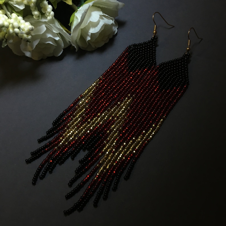 May include: Long black, red and gold beaded earrings with a fringe design.