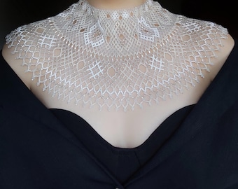 May include: A white beaded choker necklace with a delicate, intricate design. The necklace is made of small, white beads that are strung together to create a lacy pattern. The necklace is worn by a person with a black shirt.