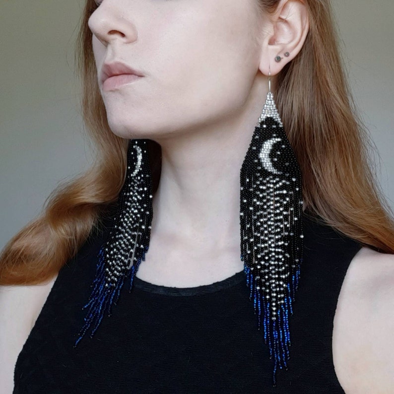 May include: Long black and silver beaded earrings with a crescent moon design and blue fringe.