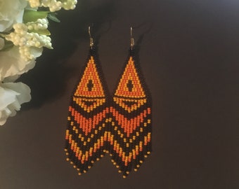 May include: A pair of long, beaded earrings with a geometric pattern in black, orange, and yellow.