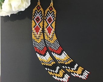 May include: A pair of long, beaded earrings with a geometric pattern in black, white, red, and yellow.