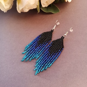 May include: A pair of long, beaded earrings with a gradient of blue and black beads. The earrings are made with small, round beads and have silver hooks.