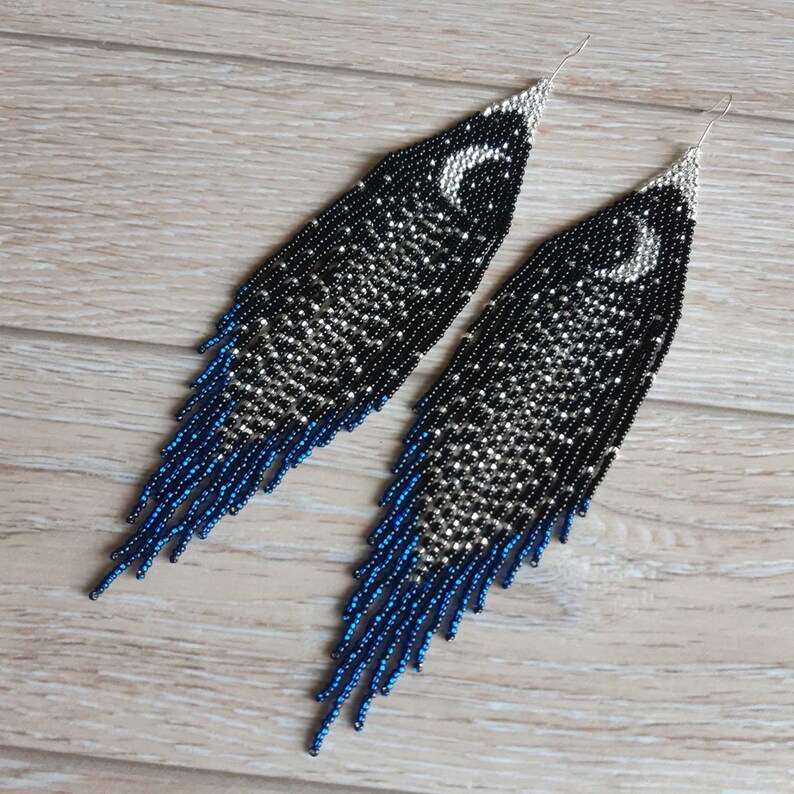 May include: A pair of long, beaded earrings with a crescent moon design. The earrings are black and silver with blue accents.
