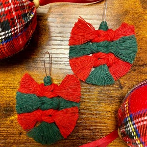 May include: Two red and green tassel earrings with a woven design. The earrings are handmade and have a festive holiday theme.