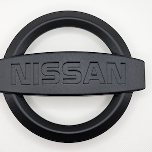 Emblema da grade Nissan escurecido (número da peça OEM: 62889-1JA0A)