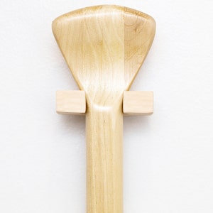 May include: A wooden paddle with a fan-shaped blade is mounted on a wall using two wooden brackets.