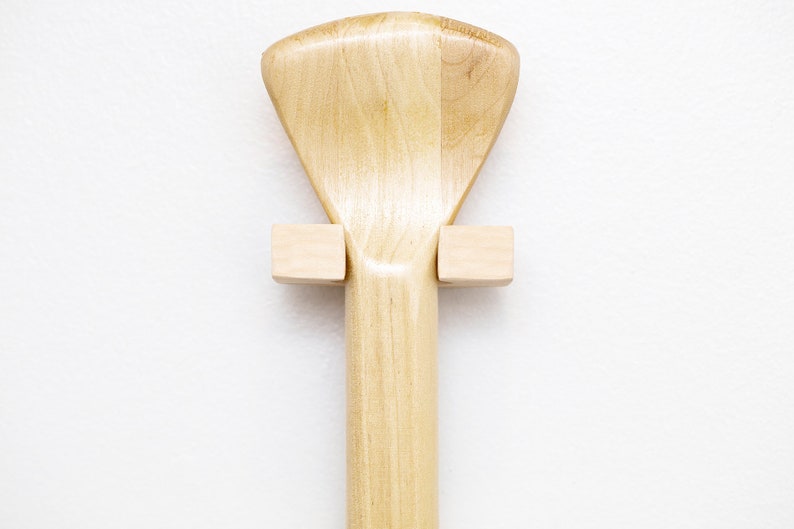 May include: A wooden paddle with a fan-shaped blade is mounted on a wall using two wooden brackets.