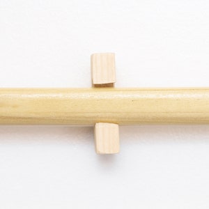 May include: A wooden dowel rod with two small wooden blocks attached to it. The blocks are positioned perpendicular to the rod.