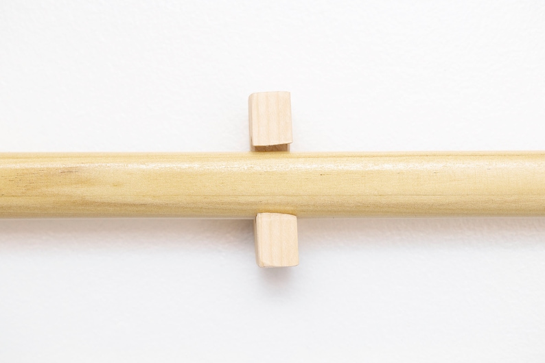 May include: A wooden dowel rod with two small wooden blocks attached to it. The blocks are positioned perpendicular to the rod.