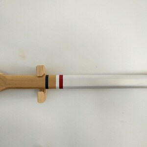 May include: A wooden oar with a white painted section and two red stripes. The oar is mounted on a wooden stand.
