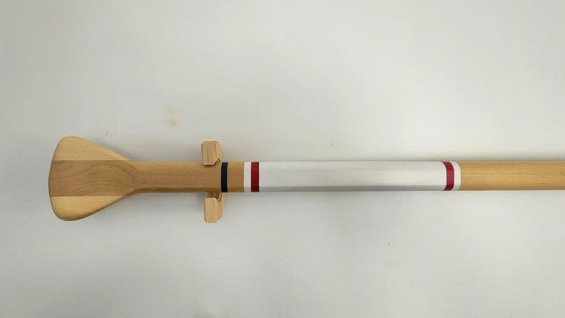 May include: A wooden oar with a white painted section and two red stripes. The oar is mounted on a wooden stand.