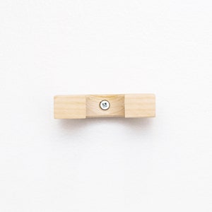 May include: A wooden wall mount with a screw in the center. The mount is light brown and has a rounded shape.