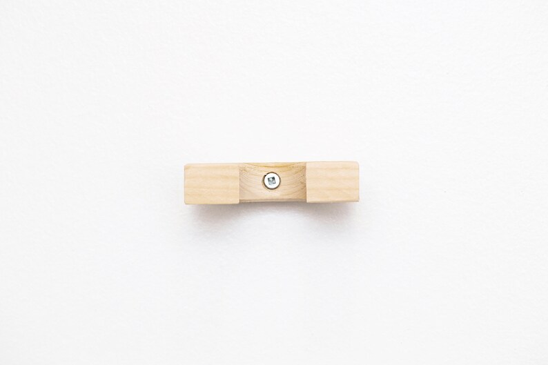 May include: A wooden wall mount with a screw in the center. The mount is light brown and has a rounded shape.