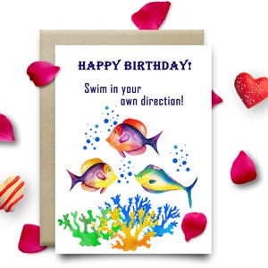May include: Happy birthday card featuring a colourful watercolour illustration of three fish swimming in the ocean with coral reefs. The card reads "Happy Birthday! Swim in your own direction!"