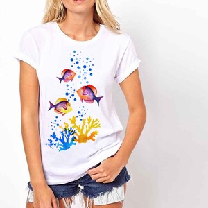 May include: White t-shirt featuring a colourful design of fish swimming through bubbles and coral. The fish are orange, yellow, blue and purple.