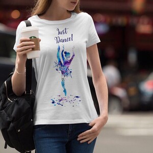 以下が含まれることがあります： 水色のバレリーナが水彩画で描かれた白いTシャツ。Tシャツには「Just Dance!」の文字がプリントされています。
