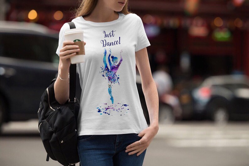 以下が含まれることがあります： 水色のバレリーナが水彩画で描かれた白いTシャツ。Tシャツには「Just Dance!」の文字がプリントされています。