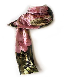 May include: A luxurious scarf in shades of pink, black, and green. The scarf features a floral design with gold accents. The fabric appears to be velvet or a similar soft material, draped against a white background.