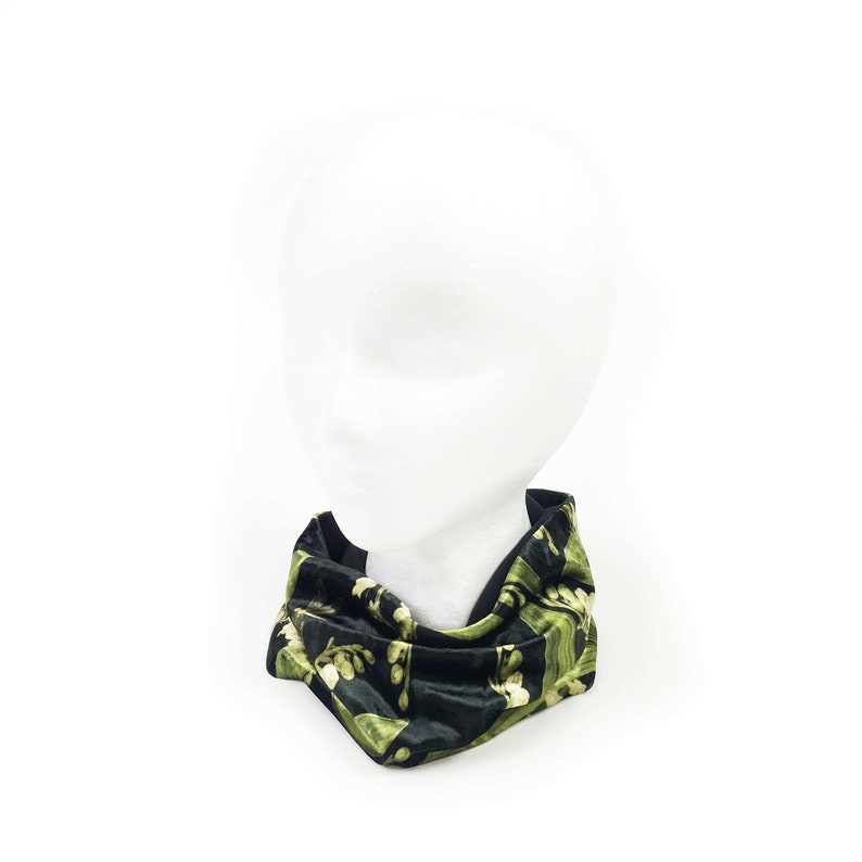 May include: A black velvet neck warmer with a green floral pattern. The neck warmer is folded and displayed on a white mannequin head.