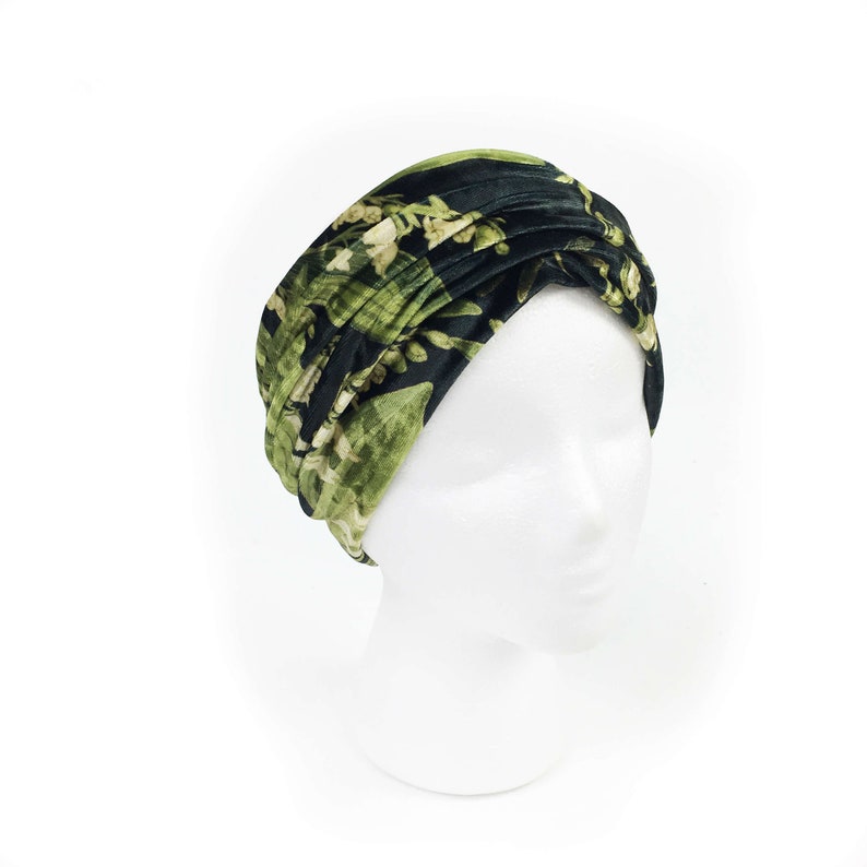 May include: A black and green floral print turban headband. The headband is made of a soft, velvet fabric and is designed to be worn as a stylish accessory.