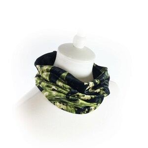May include: A black and green patterned neck warmer made of velvet. The neck warmer is folded and displayed on a white mannequin.