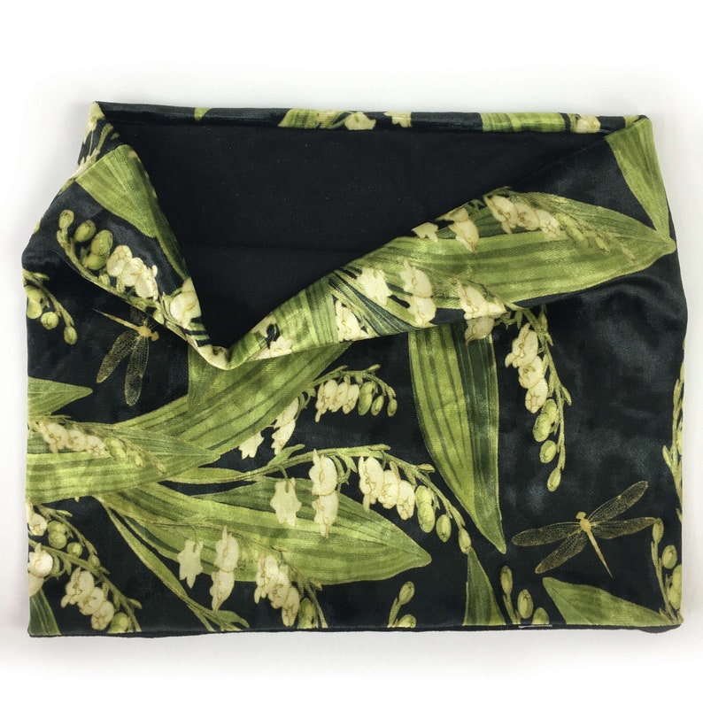 May include: Black velvet neck warmer with a green and white floral pattern featuring lily of the valley and dragonflies.
