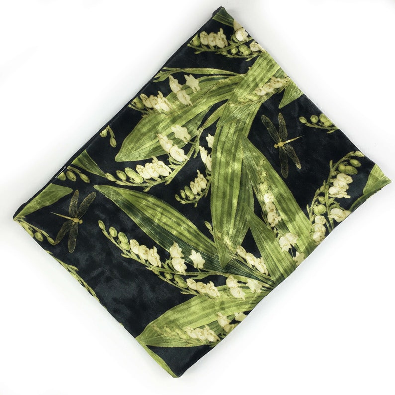 May include: A black velvet clutch bag with a floral print of lily of the valley and dragonflies. The flowers are in shades of green and white.